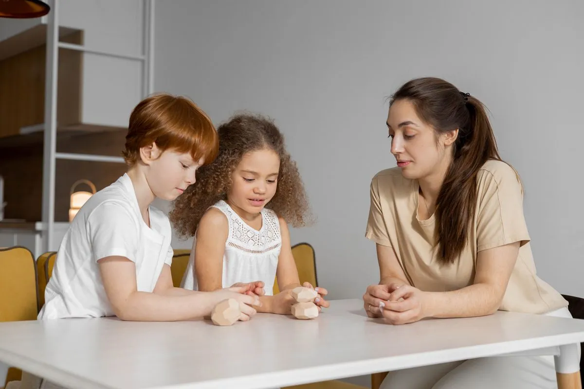 Una babysitter gioca con due bambini usando costruzioni di legno al tavolo di casa
