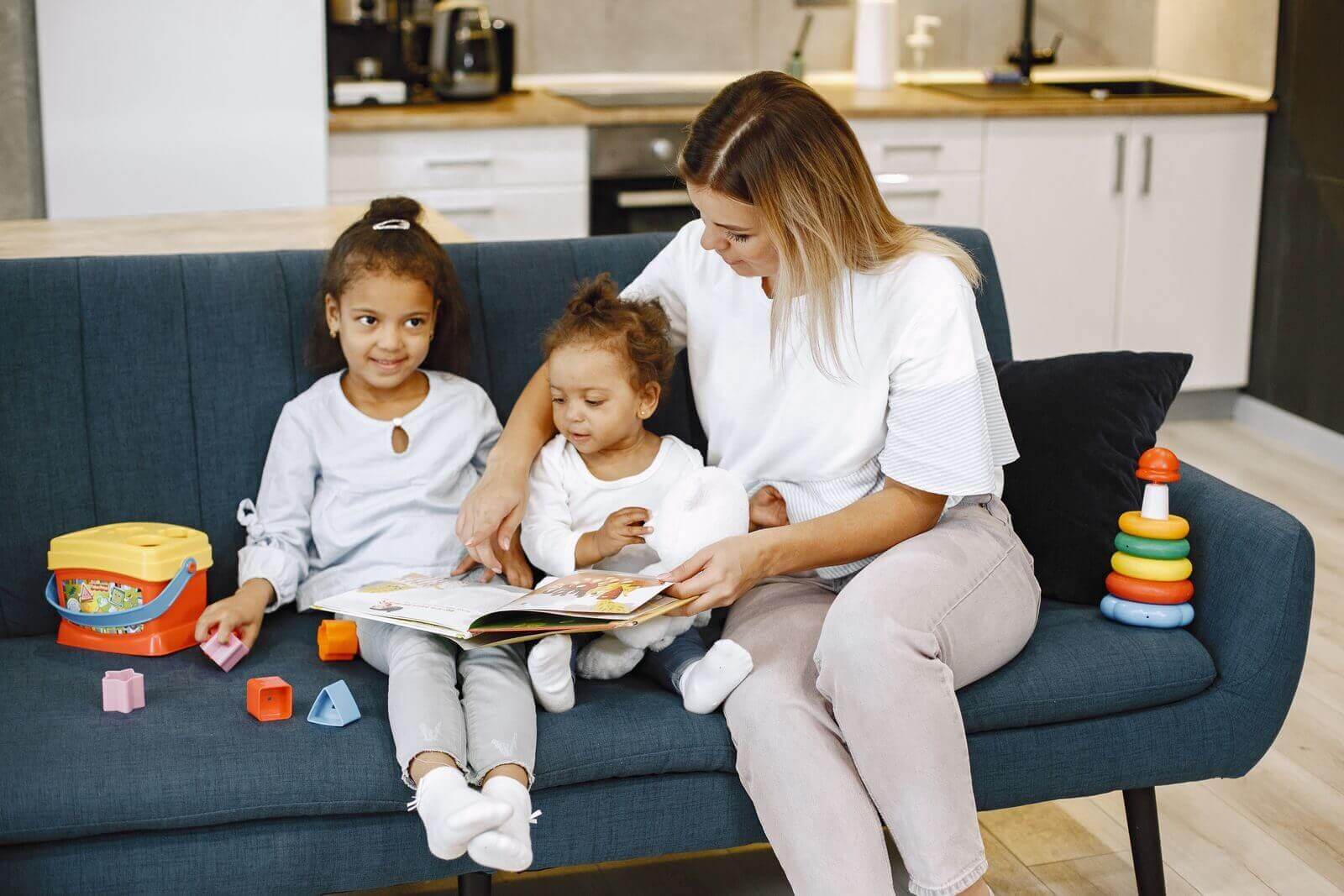 Una babysitter legge un libro a due bambini seduti sul divano di casa