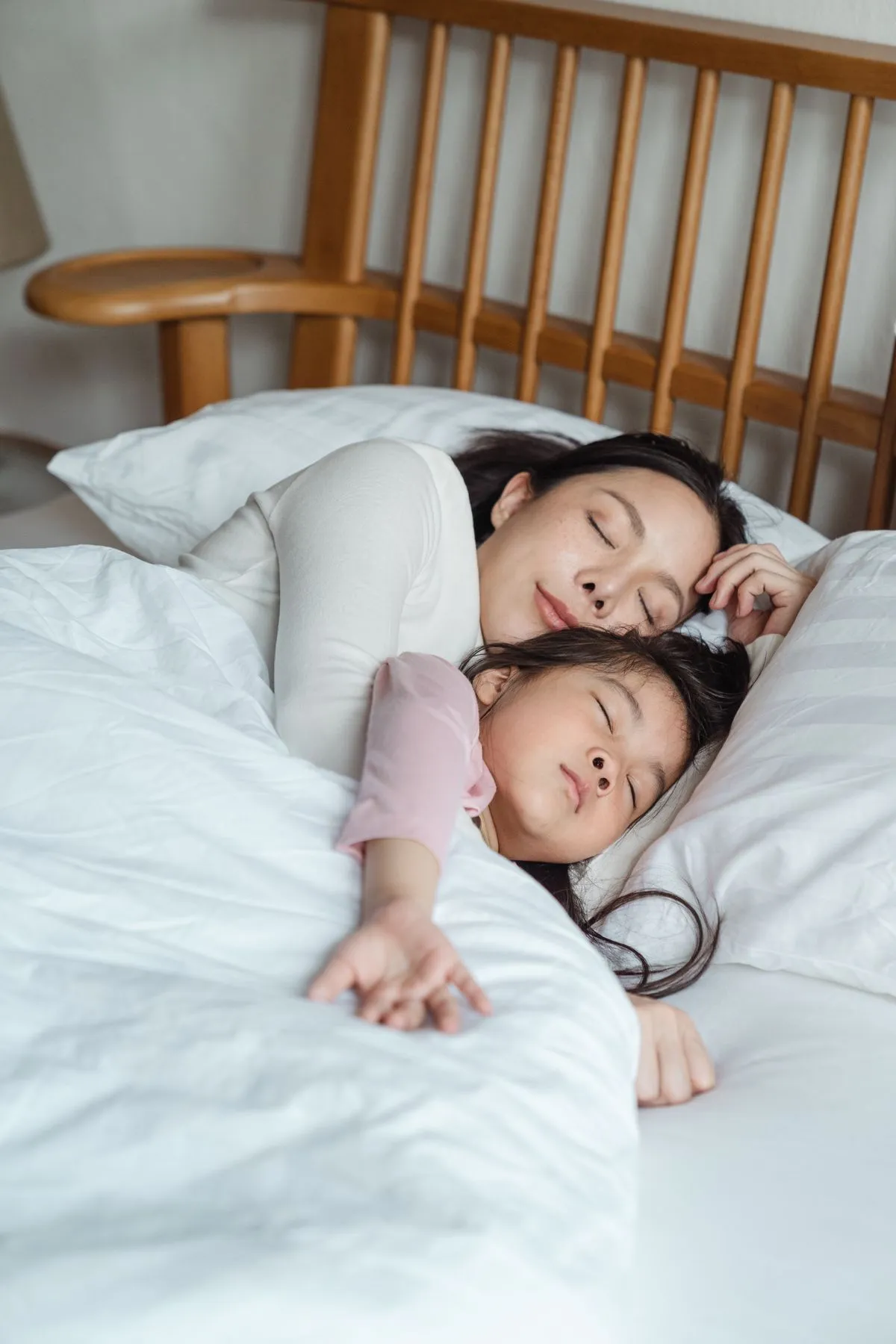 Una bambina dorme serena accanto a un adulto, avvolta nelle coperte con luce soffusa
